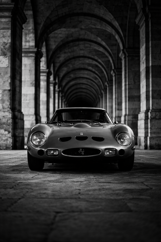 Zwart-wit foto van een klassieke Ferrari sportwagen onder bogen met symmetrische architectuur, luxe wanddecoratie.