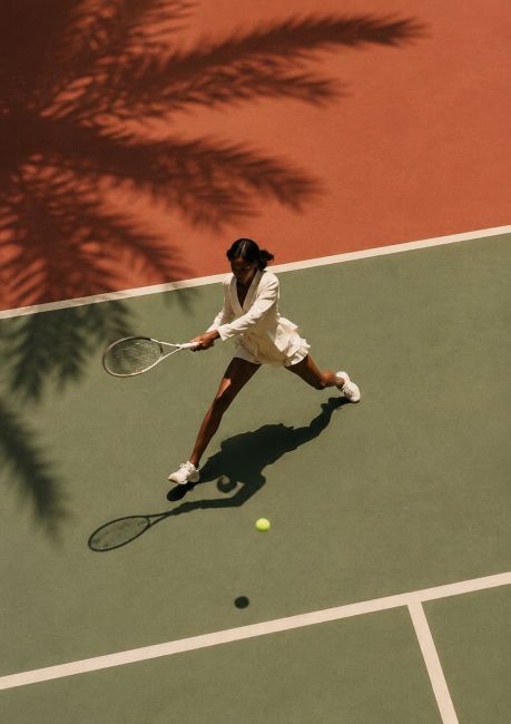 Moderne wanddecoratie van een tennisspeelster op een luxe tennisbaan met palmboomschaduw en terracotta achtergrond.