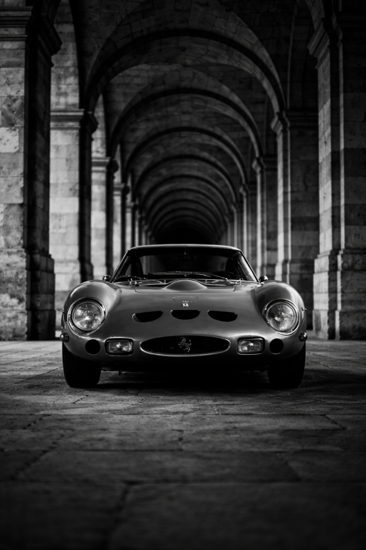 Zwart-wit foto van een klassieke Ferrari sportwagen onder bogen met symmetrische architectuur, luxe wanddecoratie.