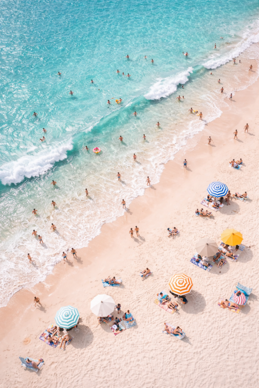 Bovenaanzicht van een druk strand met turquoise zee, zonaanbidders en kleurrijke parasols als moderne strand wanddecoratie.