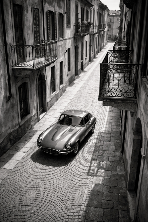 Zwart-wit foto van een klassieke vintage auto in een smalle Italiaanse straat met balkons en oude architectuur.